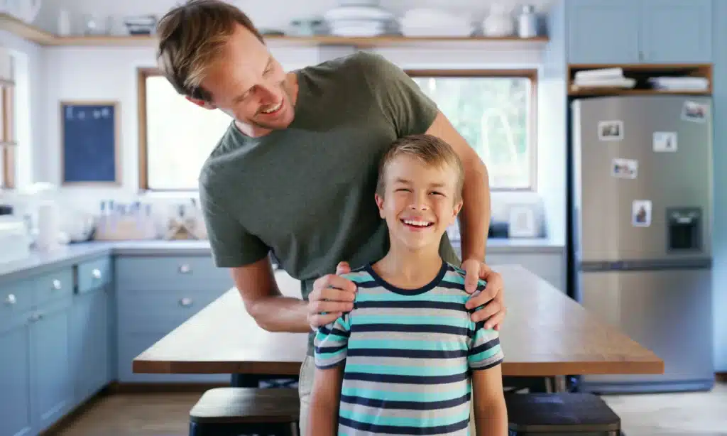 Smiling father with his hands on his son's shoulders in their home kitchen, reflecting a strong parental bond