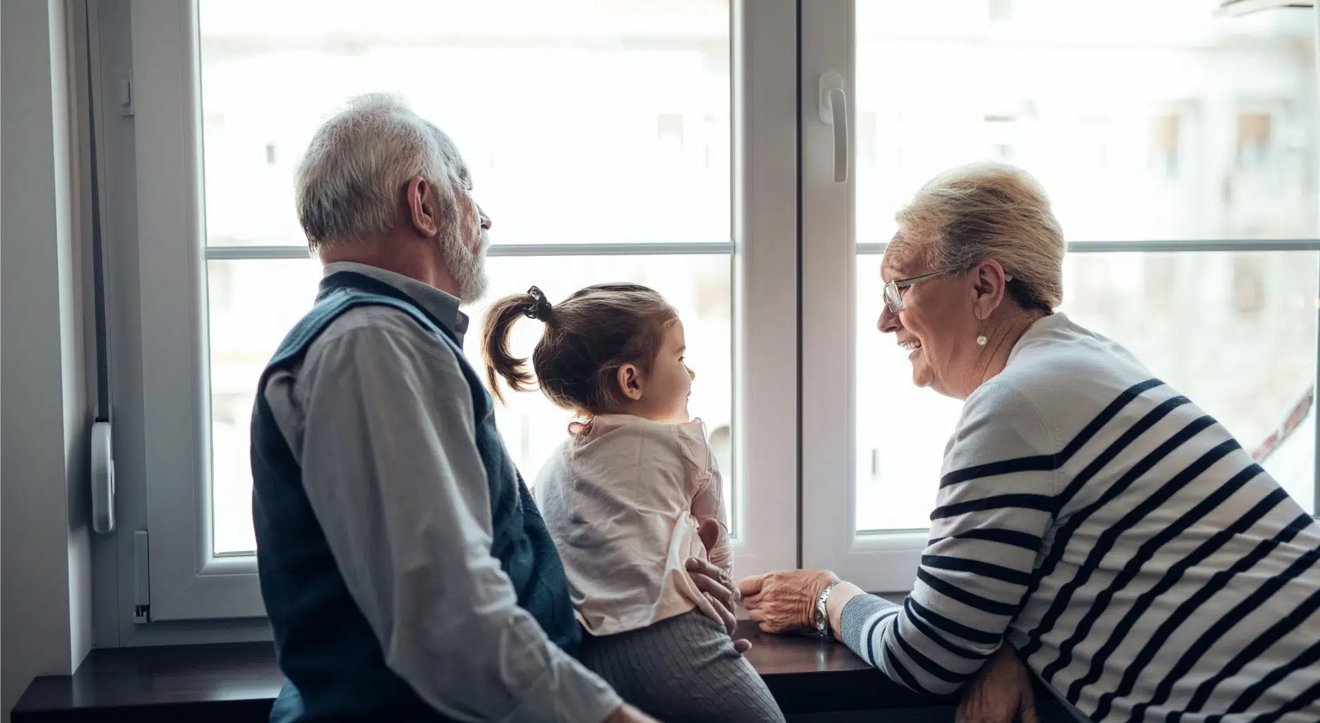 Two grandparents interacting with a grandchild while looking out a window