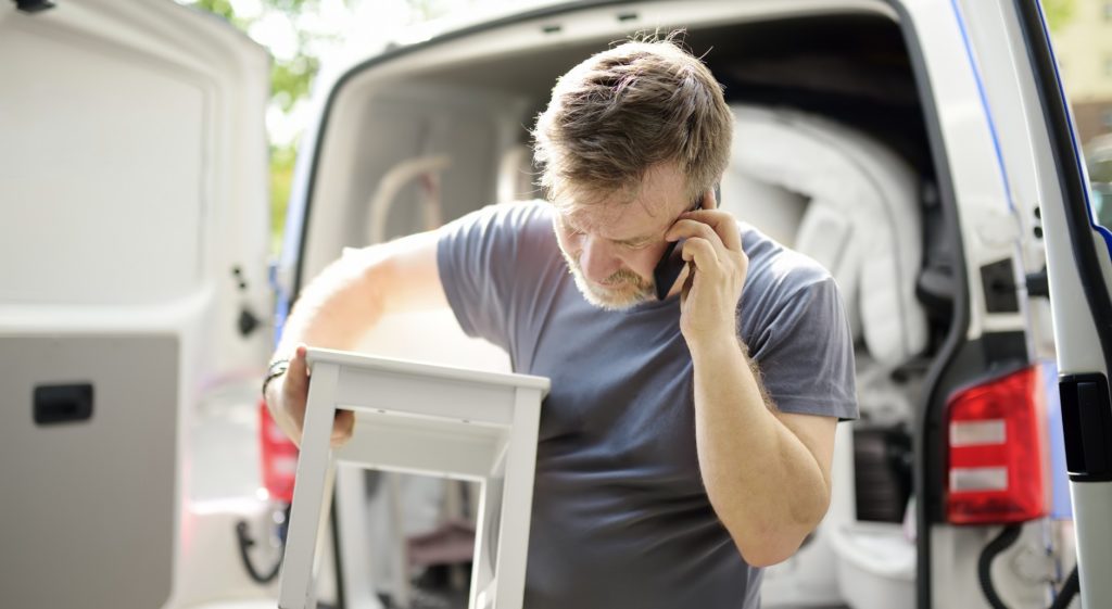 Man talks on phone while unloading white side table out of van