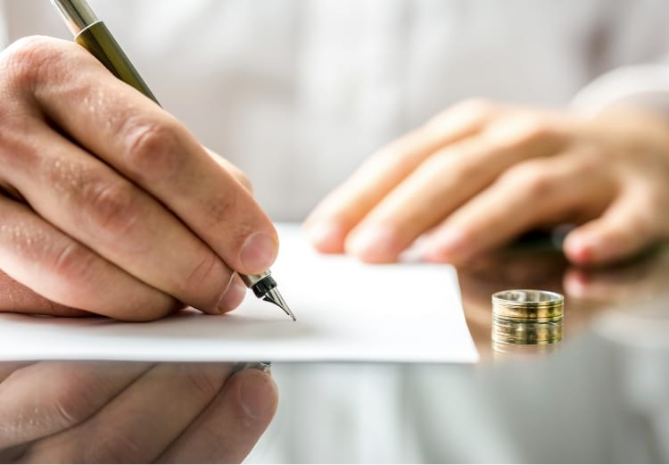 Close-up of hands signing a document with a wedding ring on the table