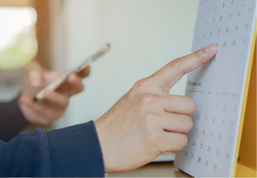 Close-up of a finger pointing to a calendar while the other hand is making a phone call