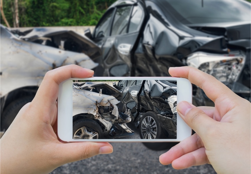 A closeup of a cell phone being used to photograph damage from a car accident involving an uber