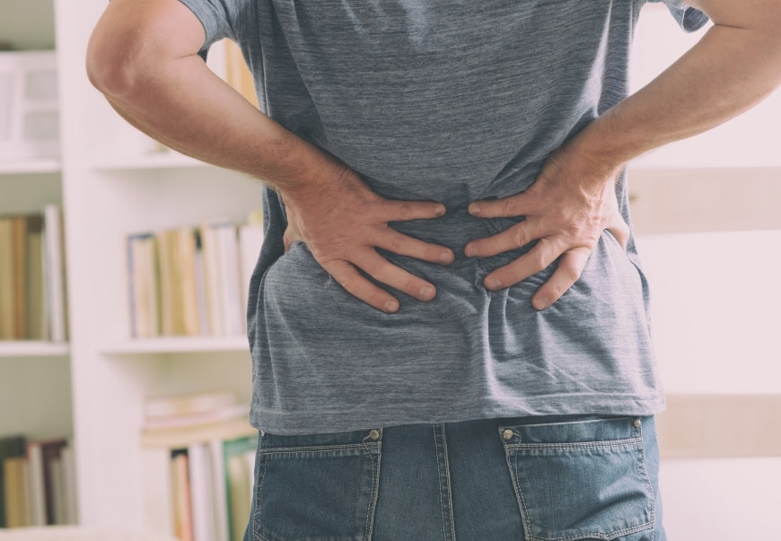 A person standing with their hands on their back indicating pain or strain