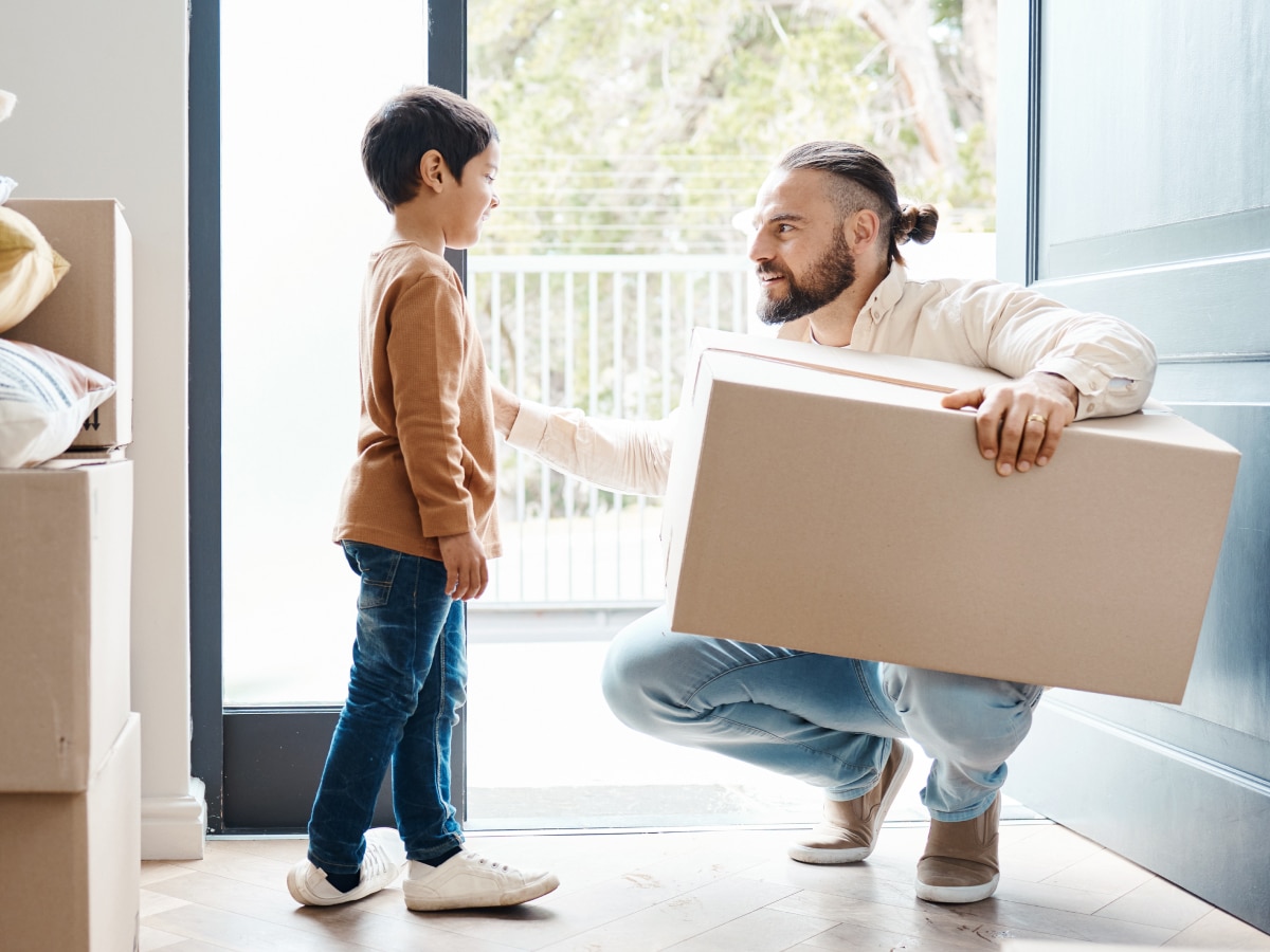 How Far Can a Parent Move with Joint Custody in North Carolina? 31 Father holding a cardboard moving box smiling at his young son during a home relocation
